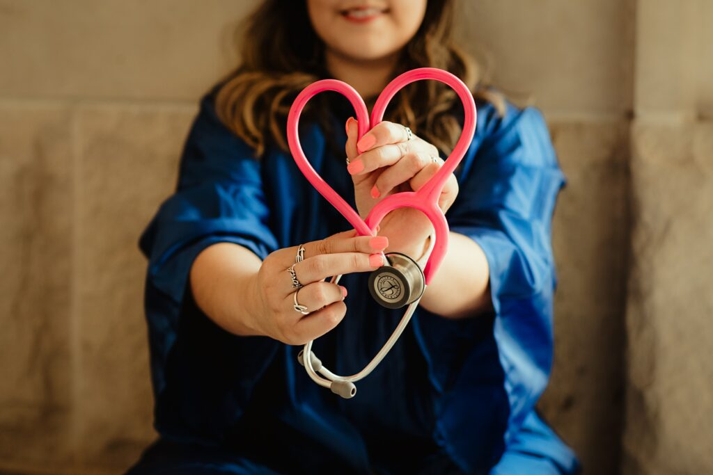 Nurse in dark blue scrubs, holding a pink stethoscope in a heart shape | Bozeman Health Infor Cloud