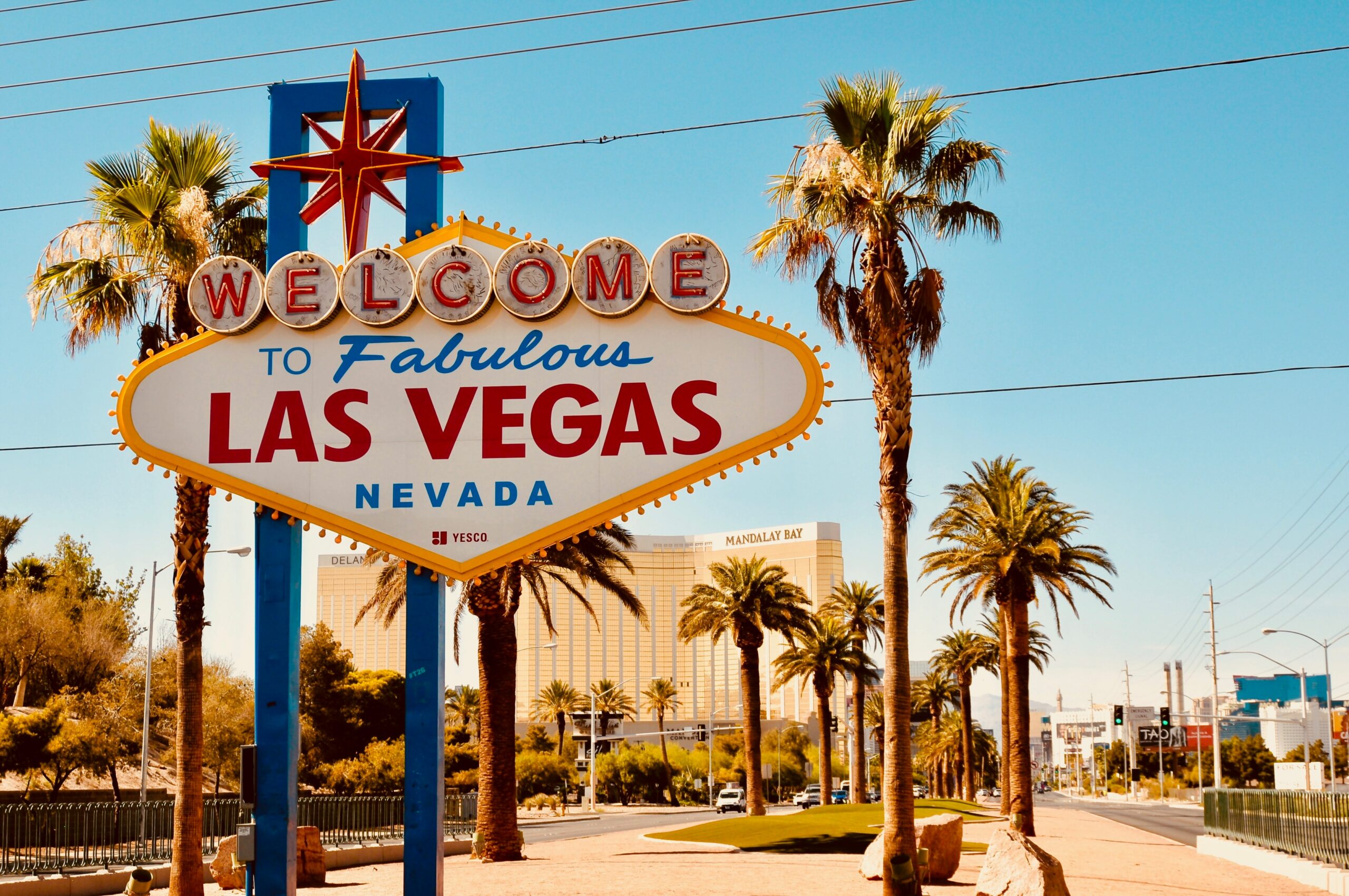 The Welcome to Las Vegas sign, with a hotel and palm trees in the background, the sky is blue and without clouds | Opkey CloudWorld