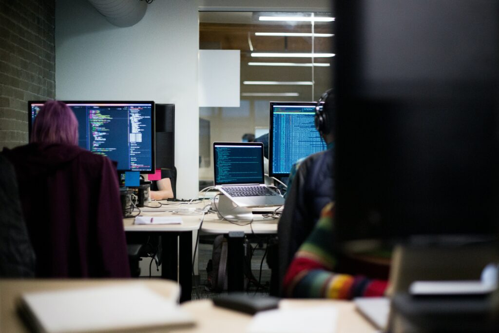 Two people have their backs to the viewer in an office setting, working on complex coding on their computers | Infor testing