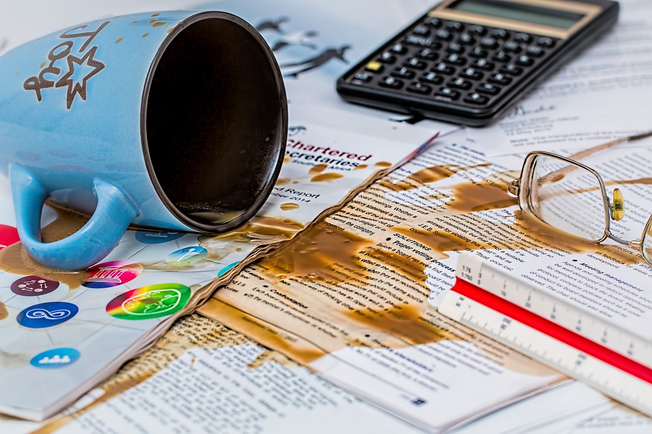 A mug of coffee that's been spilt over papers, glasses and a calculator | ERP Implementation