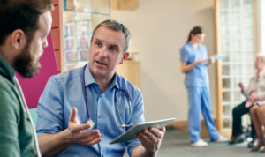 A healthcare professional speaking with a patient in a healthcare location, holding a tablet device | Oracle healthcare