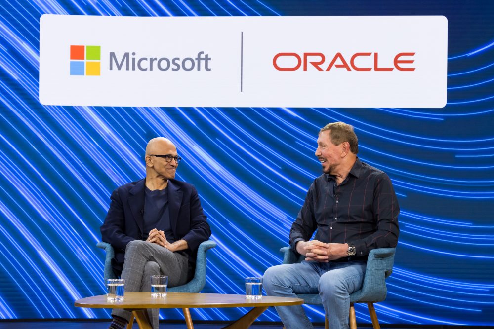 Satya Nadella, chairman and CEO of Microsoft and Larry Ellison, chairman of the board and chief technology officer of Oracle sat against a blue background speaking to one another | Oracle Database@Azure