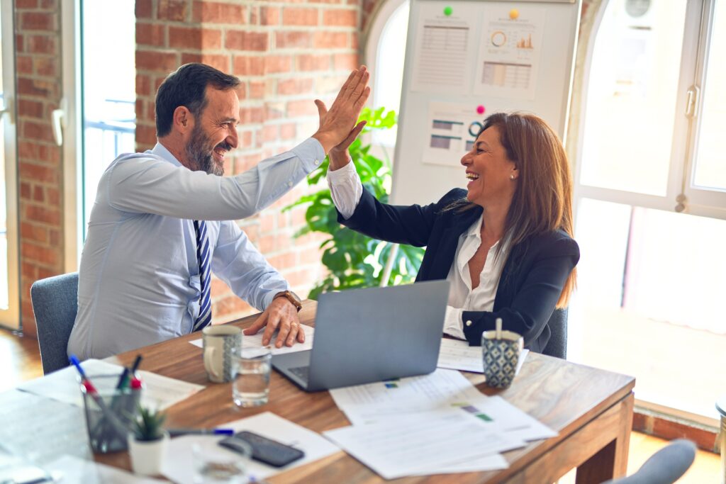 A man and a woman, both in business attire, high-fiving at a desk, with smiles on their faces | Oracle Partner Award Inoapps