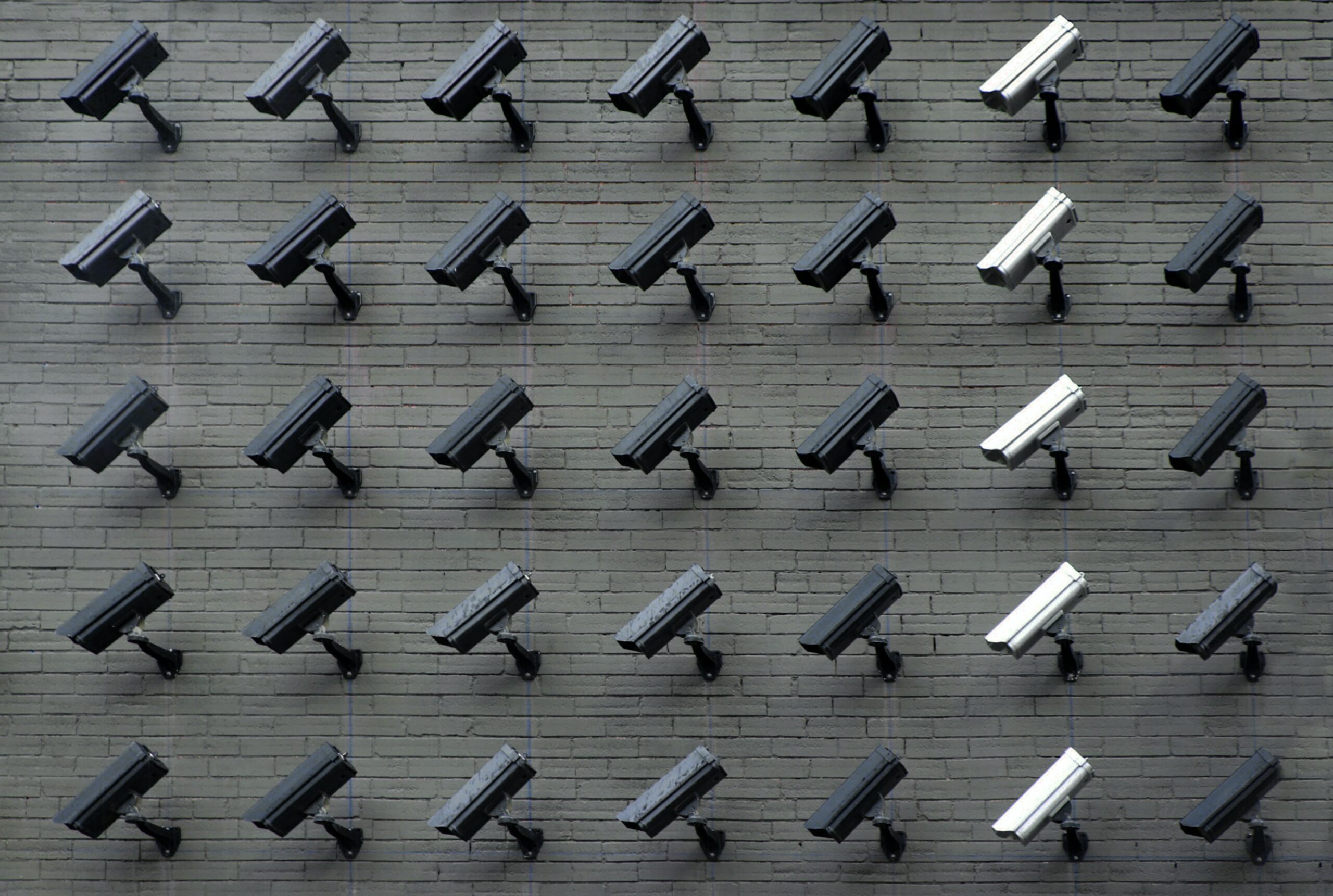 Many security cameras situated on a wall, one line of cameras to the right-hand side are white | IBM
