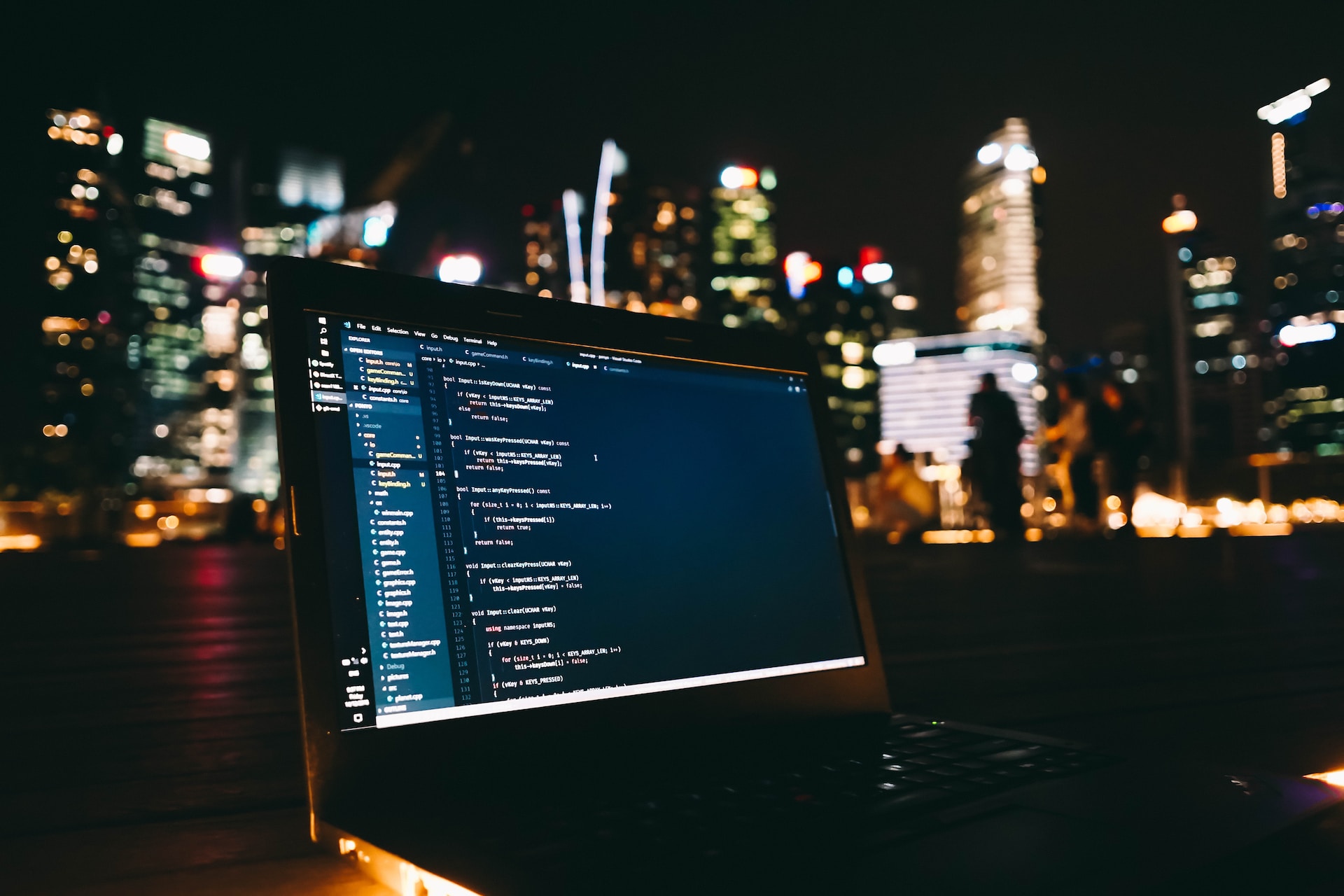 image of laptop with code on screen with buildings in the background at night time | Anypoint Code Builder