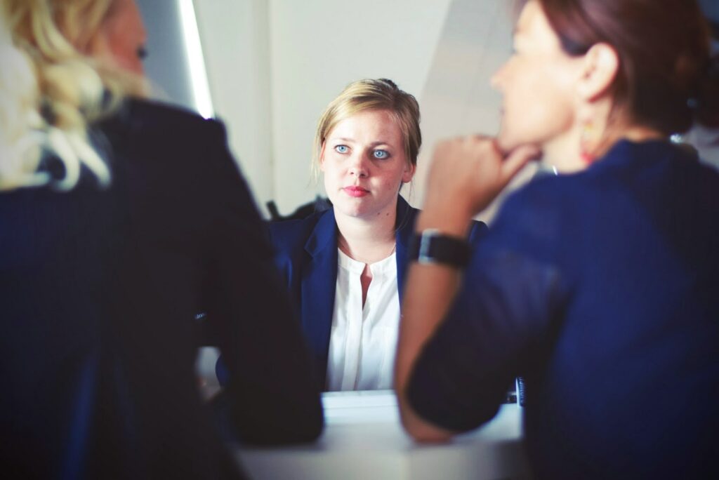 A businesswoman mediating a dispute between 2 other businesswoman sitting at a desk | ERP Implementation Sysdoc