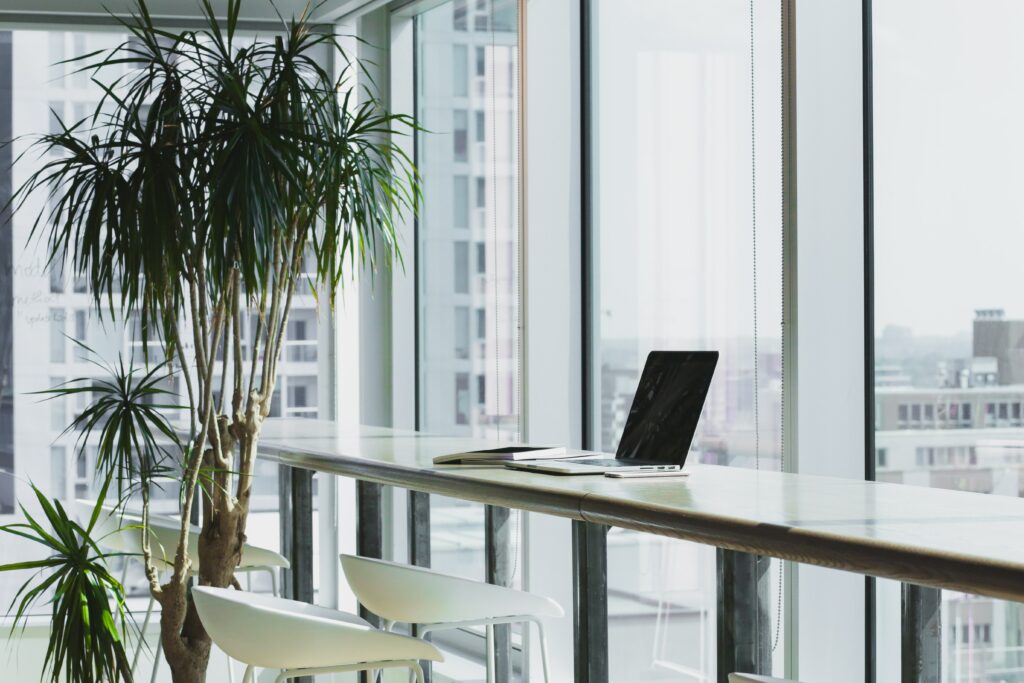 A high-rise view of several skyscrapers, with a desk and stools accompanied by a laptop and a tall plant | Boomi