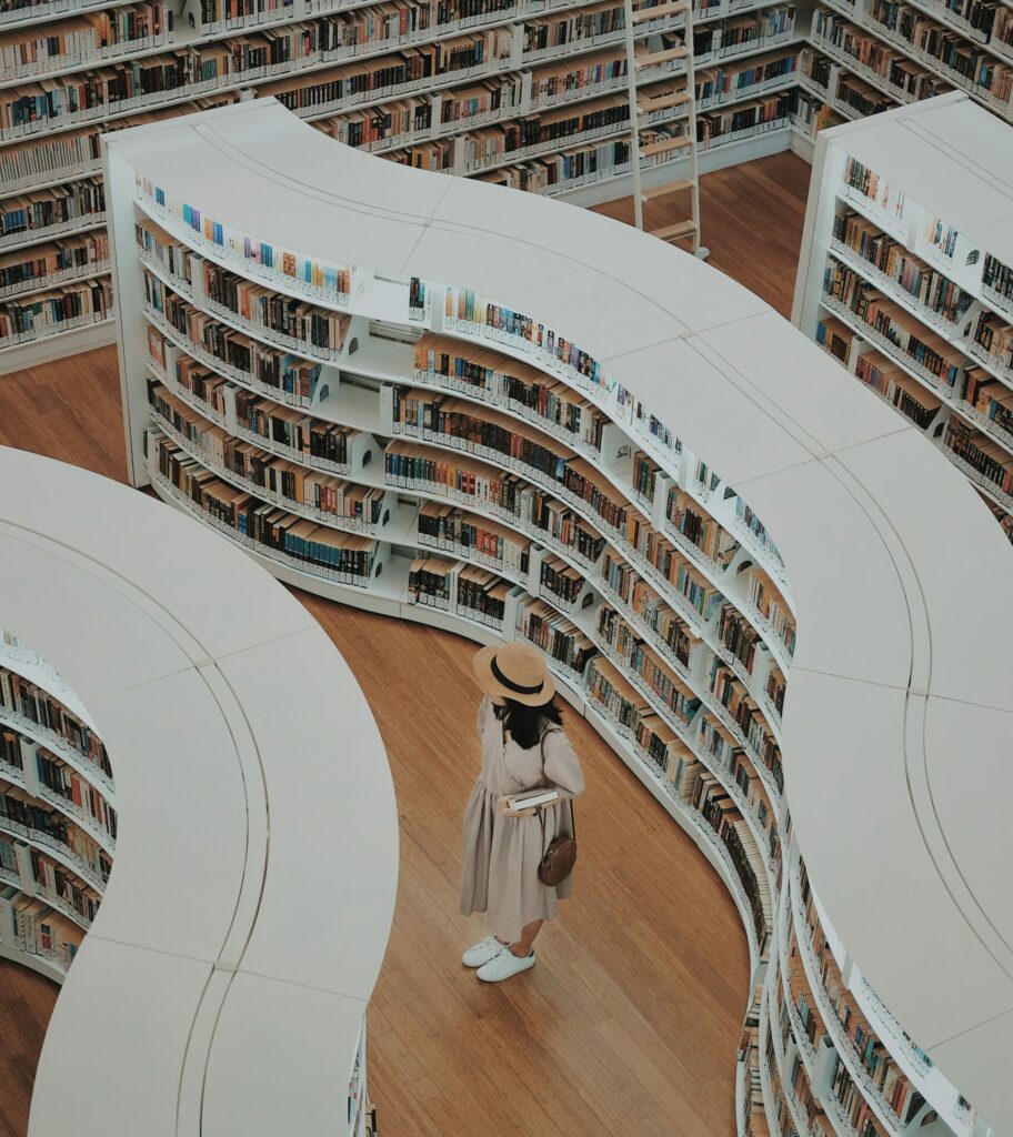 Image of a woman in a library with white wavy shelves, looking at the books on offer.