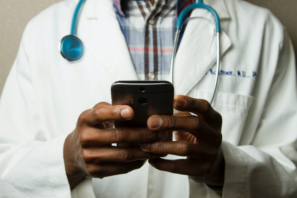 Doctor wearing his coat and with a stethoscope around his neck examines a phone in his hands, you cannot see the doctor's head | healthcare Oracle