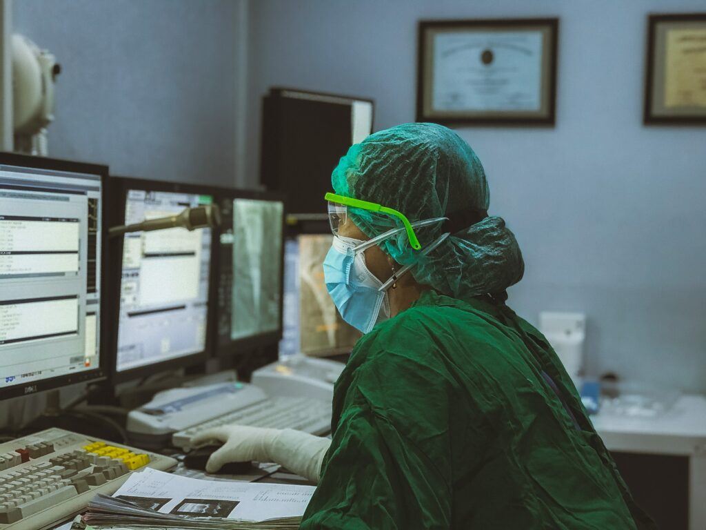 A healthcare practitioner in protective clothing works at a computer screen.