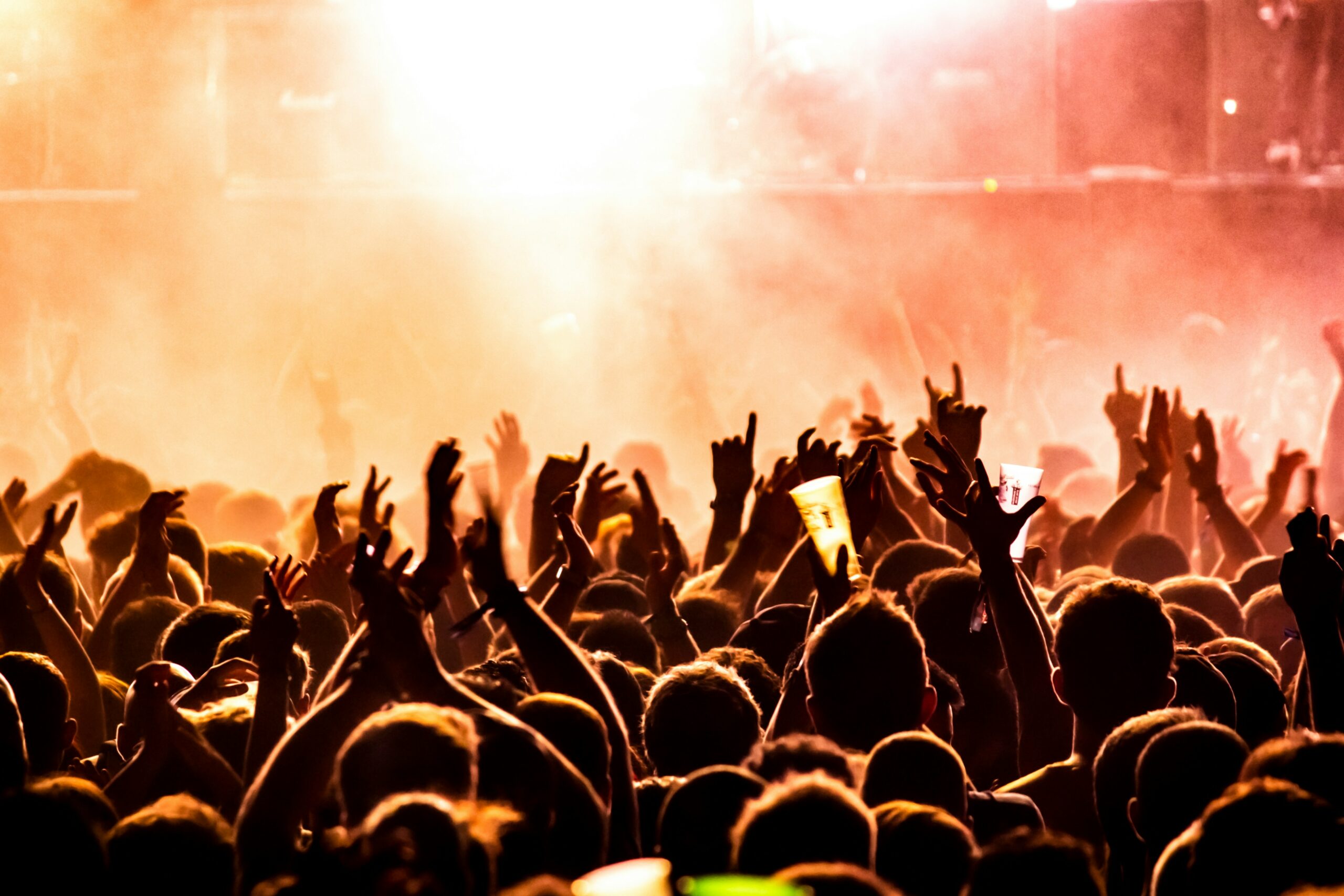 A crowd of people at a live show with their hands outstretched to the air and with bright lights shining down on the crowd | SplashBI Live Nation
