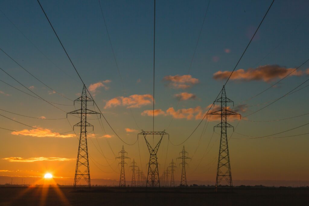 A set of power pylons against a backdrop of a sunset that gradients from blue green orange | solutions SNP