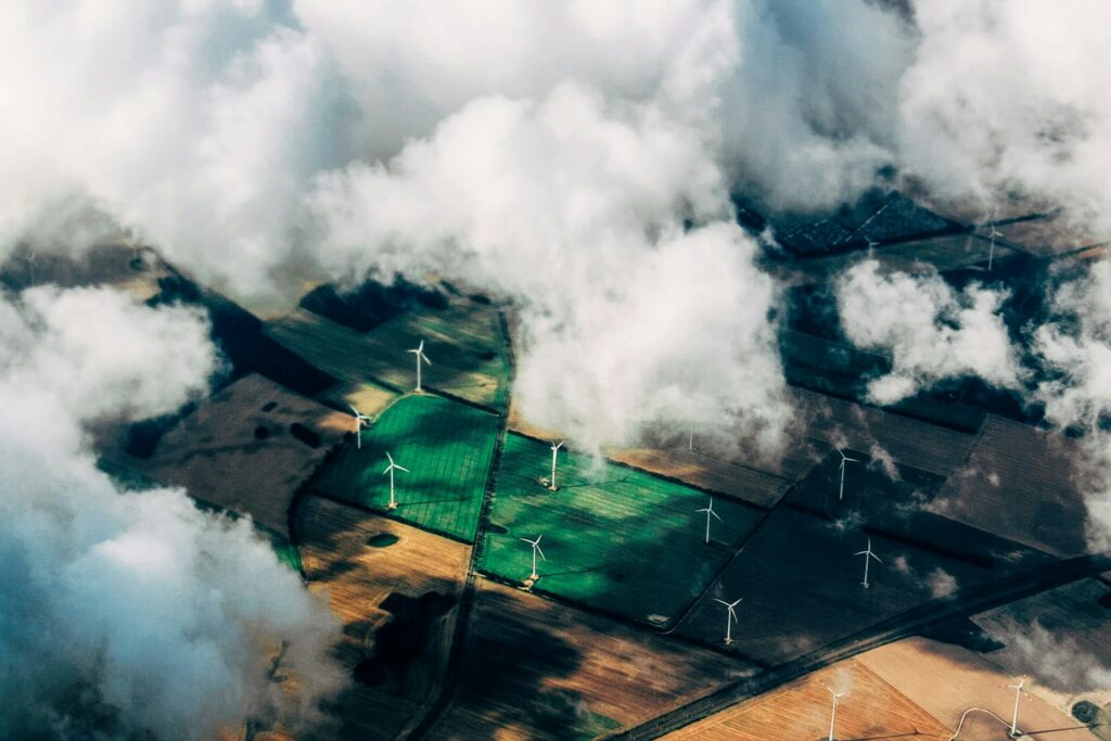 Aerial view of patchwork farmland dotted with wind turbines and slightly obscured by cloud cover | EY Sustainability