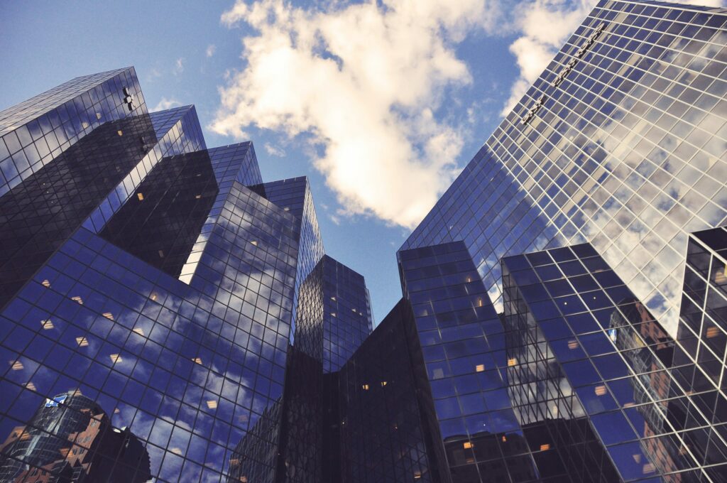 Skywards view of several black-glass buildings, reflecting the clouds above in the windows | CEOs survey EY