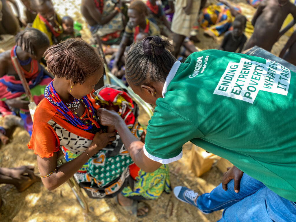 woman with a green volunteer t-shirt helping a girl with her dress | Unit4 and Embridge Consulting team up with charity Concern Worldwide