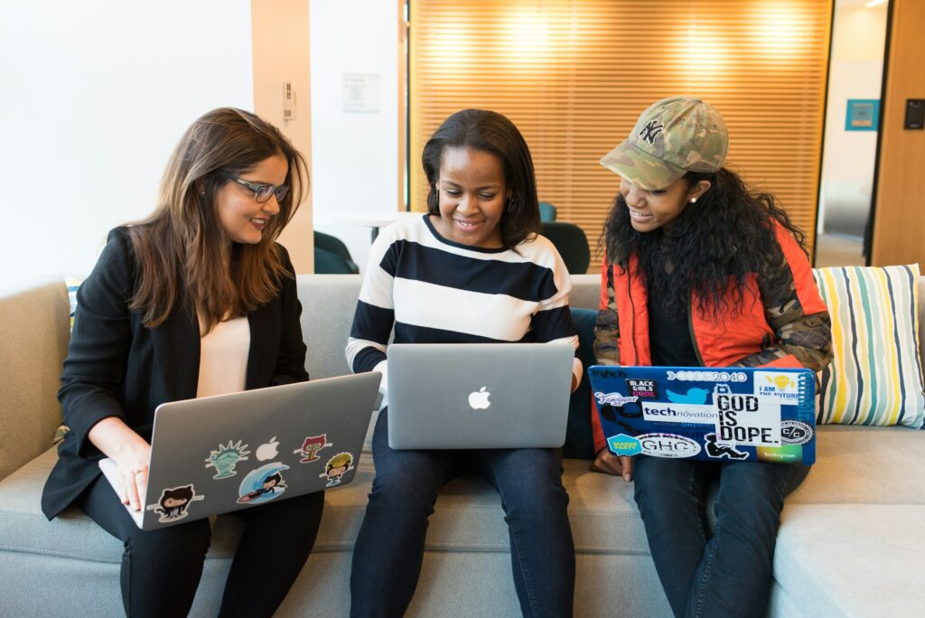 three women using laptops, smiling and talking to each other | Cognizant awards $70m to boost global tech education for diverse communities