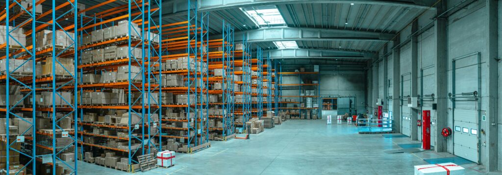 A wide-angle lens view of a warehouse with orange shelves, stacked with materials | supply chain Accelalpha