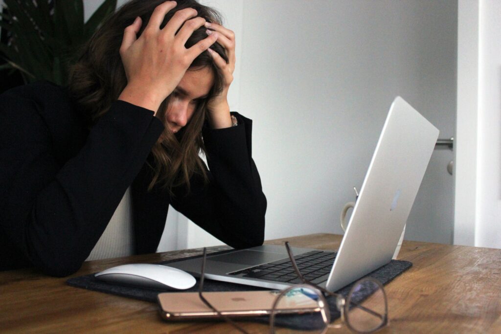 A woman sitting at a desk holding her head in frustration while looking at her laptop screen | Spinnaker Support