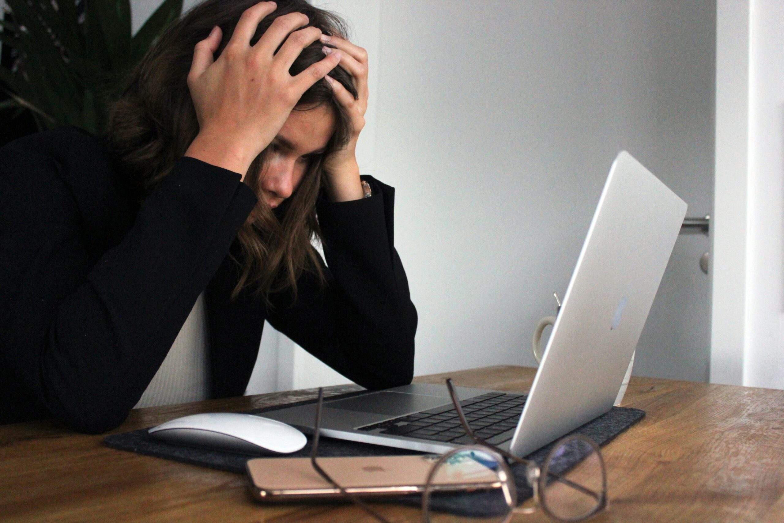 A woman sitting at a desk holding her head in frustration while looking at her laptop screen | Spinnaker Support