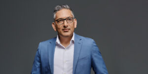 Vaibhav Vohra, new CEO of Epicor, stands confidently in a modern, blue-lit office environment.