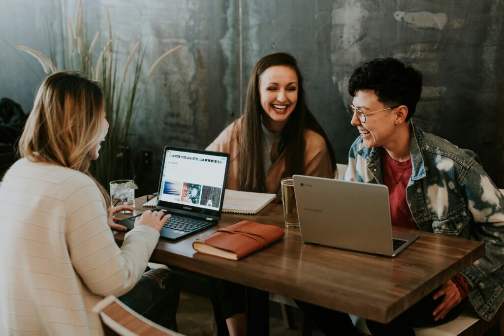 three people sitting at the table with laptops and laughing | CloudRock solution for Workday open enrollment implementation