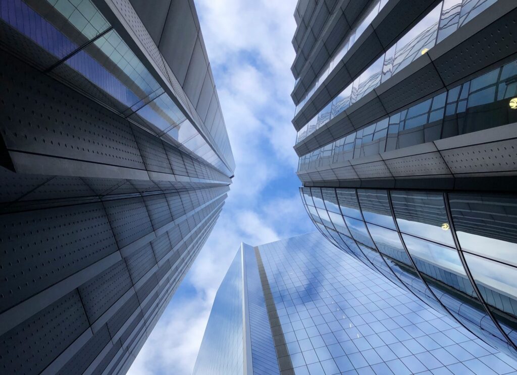 low angle photo of three high rise buildings in London with blue sky and clouds peaking from above | Rimini Street and ServiceNow partnership announcement