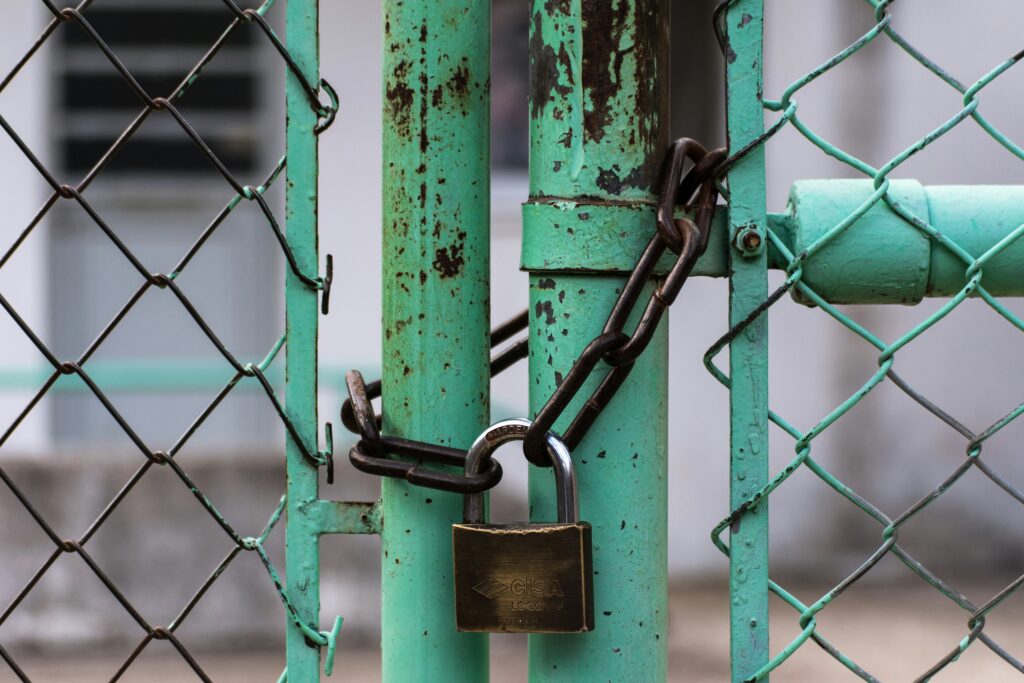 A green metal gate locked with a brass padlock |