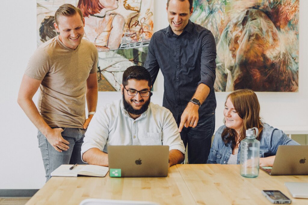 Joyful team working together and laughing, looking at a laptop with an artwork in the background | CloudRock Workday HCM add-on app