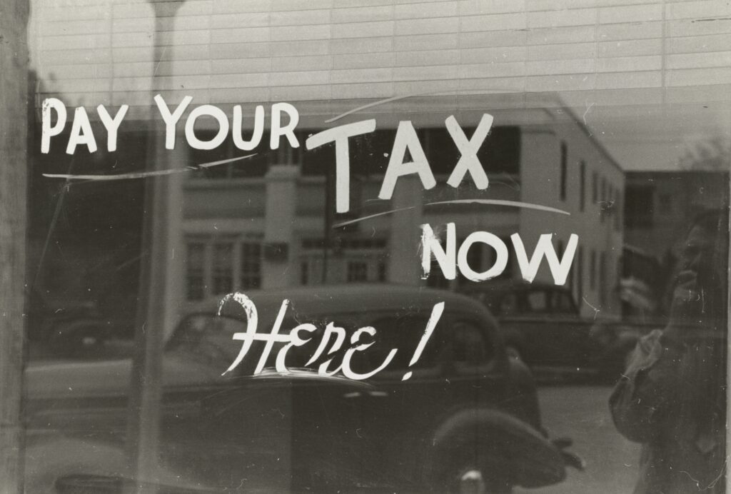 A sign on a window stating "pay your tax now here!" | CloudRock consulting solutions for Workday Financial Management Software for tax compliance