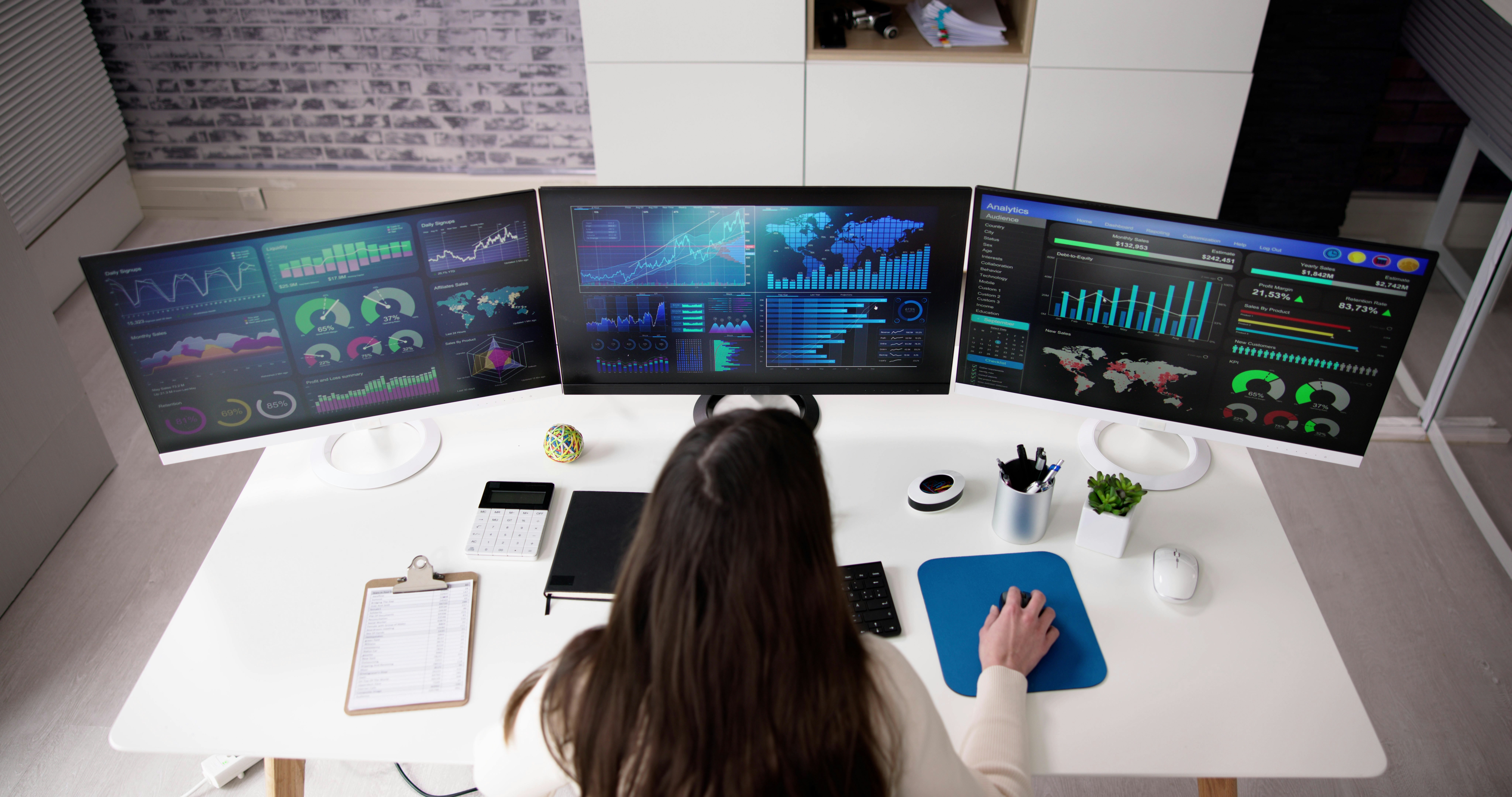 woman looking at data on three computer monitors