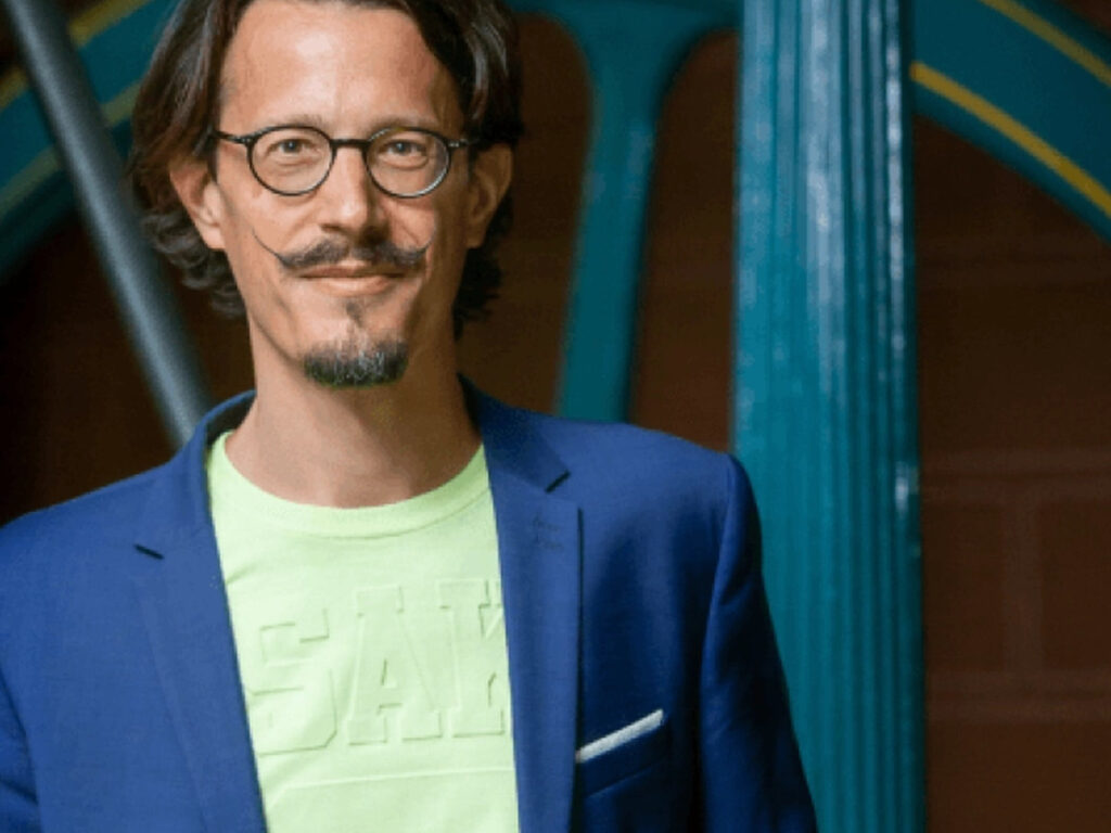 Portrait of Dr Albert Meige wearing green t-shirt and blue blazer.