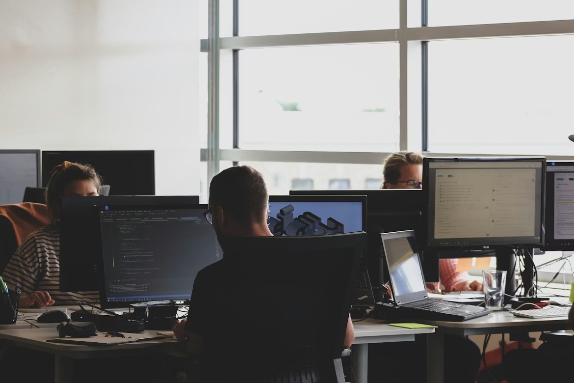 IT professionals working at computer monitors in an office, representative of enterprise system security monitoring.