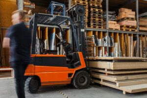 Worker with a forklift in a large carpentry workshop with many timbers in the background._SAP Ariba AI procurement