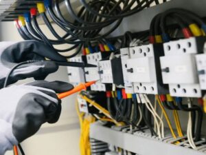 Electrical technician testing wiring and control equipment at an electrical panel