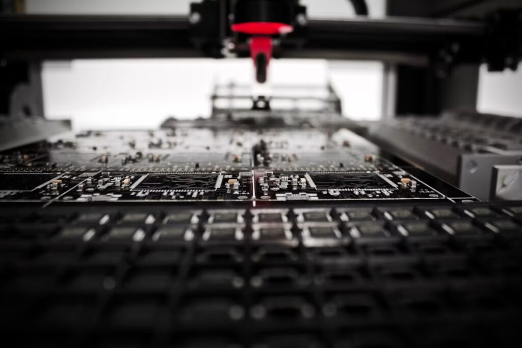 A robotic arm with a red nozzle positioned above a black circuit board in a production laboratory.