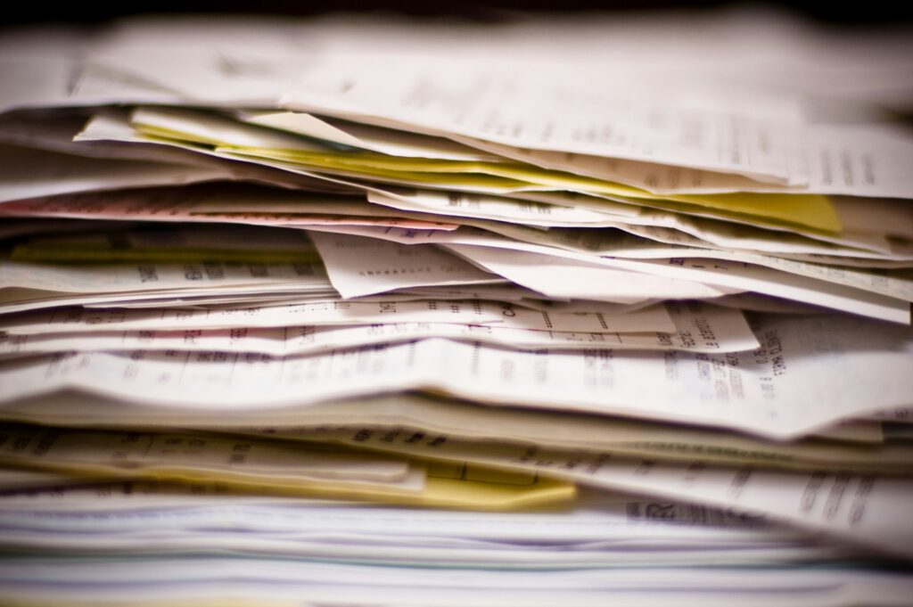 Stack of paper documents and files illustrating manual contract management, fragmented records, and paperwork-heavy procurement processes.
