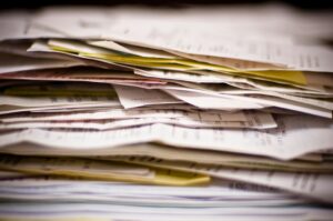 Stack of paper documents and files illustrating manual contract management, fragmented records, and paperwork-heavy procurement processes.